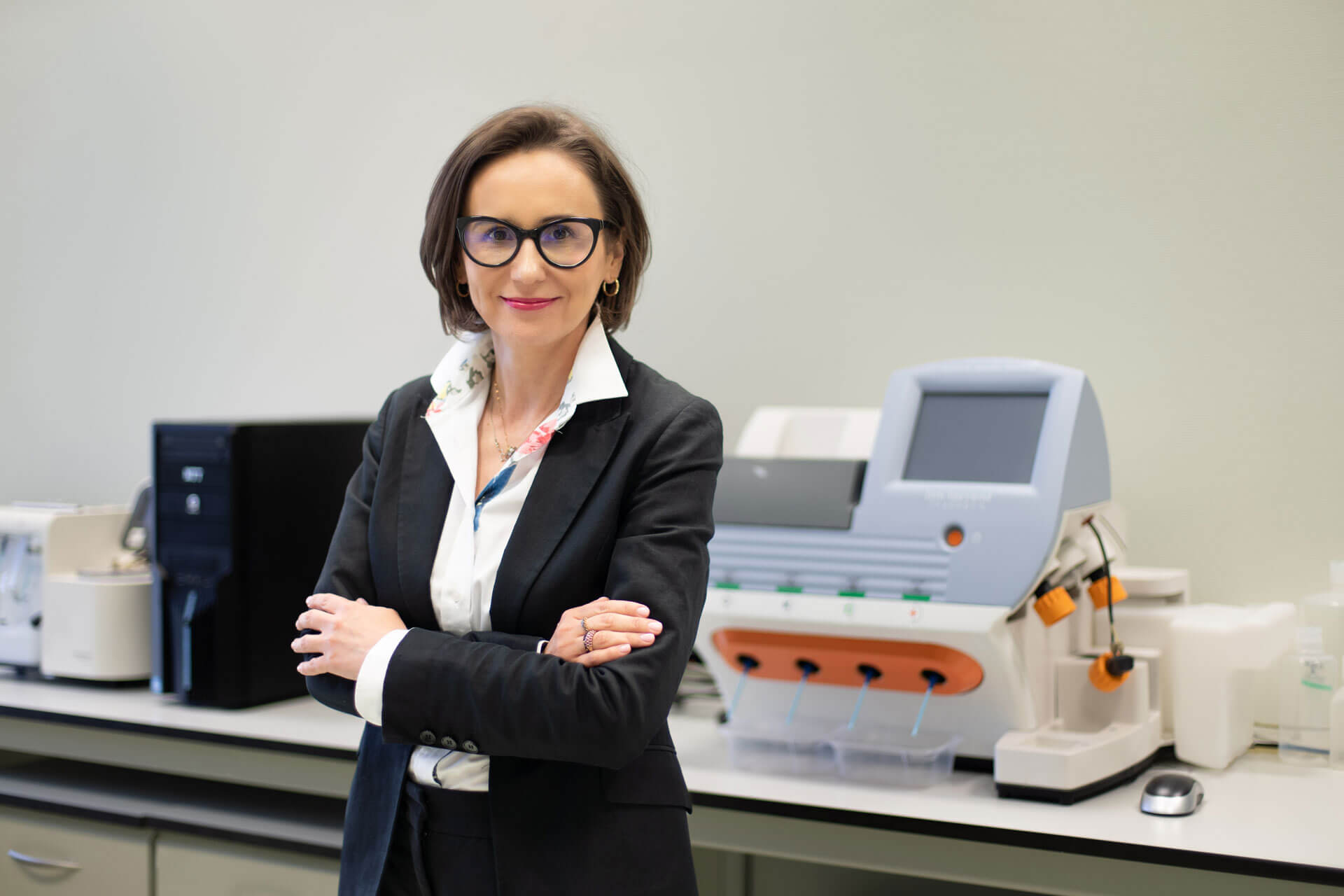 prof. Monika Czerwińska, uśmiechnięta kobieta, ubrana elegancko, stoi w pomieszczeniu laboratoryjnym