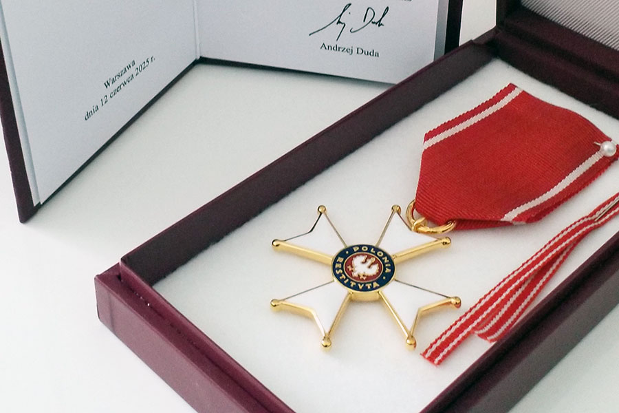 The Knight's Cross of the Order of Polonia Restituta in white, with a gold border and red ribbon. The cross is presented in a red box with white lining. Next to the box containing the order is a certificate confirming the award of the cross.
