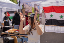 Młoda dziewczyna w czarnej czapce z daszkiem z napisem Syria. Dziewczyna klaszcze.