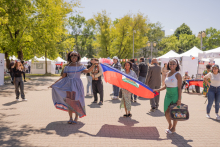 Trzy ciemnoskóre ubrane w barwne sukienki studentki niosą flagę Haiti