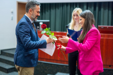 Trzy osoby. Dwie młode dziewczyny wręczają mężczyźnie kwiat - różę oraz dyplom.