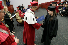 Mężczyzna w czerwonej todze wręcza dyplom kobiecie w czarnej todze.