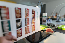Plakat ze zdjęciami różnych wypełnień zębowych, w tle stoły a na nich materiały do ćwiczeń stomatologicznych