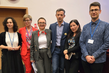 Sześć osób, cztery kobiety i dwóch mężczyzn, stojących w rzędzie. Są to organizatorzy konkursu i opiekunowie studentów. Uśmiechają się do zdjęcia. Są formalnie i nieformalnie ubrani. Tło stanowi drewniana ściana z pionowymi panelami. 