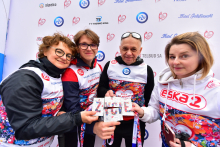 Trzy kobiety i mężczyzna stojący blisko siebie, każdy z nich trzyma jedną literę tworzącą wspólny napis „ŻYCIE”. Litery wyglądają jak elementy układanki – puzzli. Osoby ubrane są w sportowe stroje z numerami startowymi. W tle znajduje się ścianka z logotypami