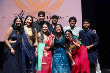 Dziewięcioro studentów i studentek WUM stoją na scenie. Za nimi znajduje się duży ekran z napisem „thank you”. Mają na sobie kolorowe, tradycyjne ubrania w odcieniach niebieskiego, czerwonego, zielonego i złotego. Uśmiechają się i pozują do zdjęcia.