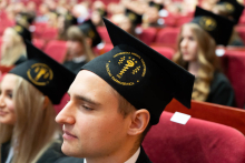 Zbliżenie na twarze absolwentów zwrócone bokiem do zdjęcia, patrzące przed siebie. Na głowach absolwenci mają czarne birety ze złotym wyhaftowanym logo Wydziału Farmaceutycznego.