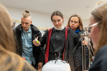 Grupa kilku osób wokół trenażera do operacji laparoskopowych. Jedna z osób - młoda dziewczyna pracuje na trenażerze. 