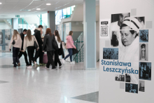 Jasny wysoki korytarz, na którym po lewej w oddali znajduje się grupa osób. Po prawej widać fragment wystawy - duża plansza, na której znajdują się teksty i czarno-białe fotografie dotyczące Stanisławy Leszczyńskiej.