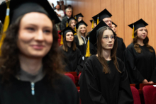 Grupa młodych osób, absolwentów farmacji, zwrócona twarzami do środka auli. Są w trakcie powtarzania słów przysięgi. Mają na sobie czarne togi i birety.