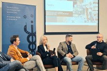 Four people sit on chairs and hold microphones during a panel discussion. In the background is a screen that reads “Panel 2” and a blue banner that reads “Warsaw Medical University Faculty of Health Sciences.”