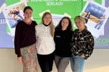 Cztery osoby stoją obok siebie na tle zielonego ekranu z napisem „DZIAŁACZEK O WIELKICH SERCACH”. Na ekranie widoczne są dwa zdjęcia: grupy osób i dwóch osób przed tablicą. Osoby ubrane są swobodnie, w jasnych i ciemnych bluzach oraz koszulach.