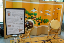 Ekspozycja tradycyjnych koreańskich instrumentów muzycznych przed ozdobnym parawanem z malowidłem żurawi i sosen. Widoczne są bęben Buk, bęben Janggu, mały gong Kkwaenggwari i duży gong Jing. Po lewej stronie tablica informacyjna w języku koreańskim i angielskim.