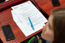 Na drewnianym biurku leżą dwa smartfony, niebieski długopis i kartki papieru. Górna kartka zawiera nagłówek „PROGRAM KONFERENCJI 2025".