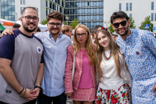 Pięć osób - trzech młodych mężczyzn i dwie kobiet stoją blisko siebie i pozują do zdjęcia. Uśmiechają się. Ubrane są w różnorodne, także tradycyjne stroje. W tle widoczne są budynki i drzewa.