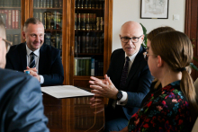 Cztery osoby przy stole w sali konferencyjnej. Jedna z nich zwraca się do pozostałych gestykulując.