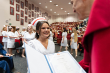 Uroczystość czepkowania absolwentów pielęgniarstwa i położnictwa. Mężczyzna w czerwonej todze wręcza dyplom młodej kobiecie w białym uniformie medycznym i czepku położnych.