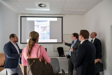 W sali konferencyjnej znajduje się pięć osób – trzy stoją, dwie siedzą – oglądają prezentację na ekranie projekcyjnym.