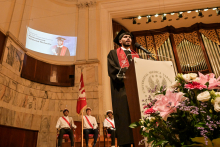 Absolwent w czarnej todze i birecie stoi przy mównicy z logo „Universitas Medica Anon”. W tle ekran z napisem „Gratulacje dla Muhammada Mostafę Metwally'ego”. Po lewej flaga i trzej mężczyźni w ceremonialnych strojach. Po prawej bukiet kwiatów.