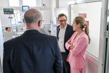 Trzy osoby w formalnych strojach rozmawiają w szpitalnym pomieszczeniu z aparaturą medyczną.