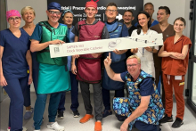 A group of women and men in a hospital corridor, dressed in medical attire, including gowns and protective lead aprons. Some of them are holding a long banner.