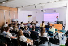 Sala wykładowa wypełniona słuchaczami, przed nimi mężczyzna i prezentacja na dużym ekranie