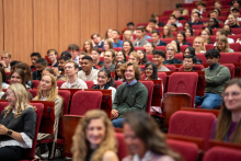 Młodzi ludzie różnych narodowości i w różnym wieku siedzą w audytorium, zwróceni w stronę sceny znajdującej się poza kadrem.