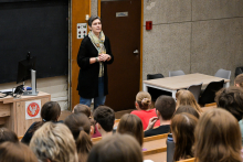 Prodziekan, ubrana nieformalnie, stoi na środku sali i przemawia. Jest zwrócona w stronę uczniów. Na przeciwko niej siedzi grupa młodych osób.