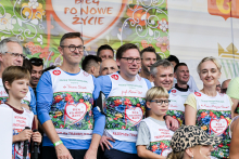 Około dwudziestu osób pozuje na tle kolorowego baneru z napisem „Bieg po nowe życie”. Uczestnicy noszą koszulki z sercem i hasłem „Razem dla transplantacji”. 