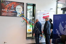 Dwaj mężczyźni i dwie kobiety trzymają kolorowe wstęgi, zawieszone na tablicy upamiętniającej Andrzeja Kraśnickiego. W tle widoczne logo Polskiego Komitetu Olimpijskiego i baner Warszawskiego Uniwersytetu Medycznego.