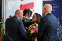 Cztery osoby w eleganckich strojach stoją razem, wymieniają uściski i kwiaty.