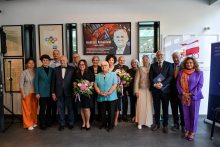 Piętnaście osób pozuje do zdjęcia w jasnym pomieszczeniu. Kilka osób trzyma bukiety kwiatów. W tle trzy plakaty, w tym jeden z wizerunkiem Andrzeja Kraśnickiego (1949–2025) i napisem upamiętniającym jego życie.