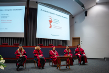 Pięć osób w togach siedzi na scenie podczas uroczystości dyplomatorium.