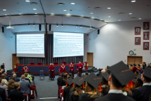 Sześć osób w togach na scenie podczas uroczystości wręczenia dyplomów; przed nimi stoją absolwenci w biretach. i składają ślubowanie.