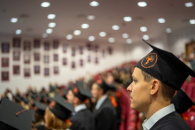 Grupa absolwentów w togach i biretach siedzi w audytorium podczas uroczystości ukończenia studiów.