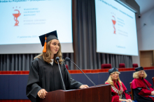 Osoba w todze przemawia przy mównicy podczas uroczystości dyplomatorium