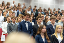 Duża grupa elegancko ubranych młodych kobiet i mężczyzn. Stoją w auli i przyjmują ślubowanie.