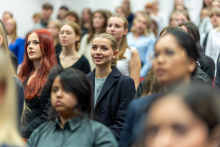 Duża grupa elegancko ubranych młodych kobiet i mężczyzn. Stoją w auli i przyjmują ślubowanie.