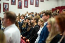 Studenci w czasie składania przysięgi. Są to osoby młode, nieformalnie ubrane. Wyglądają na skupione. Patrzą przed siebie. Stoją w równych rzędach w auli.