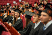 Absolwenci w togach i biretach z pomarańczowymi frędzlami siedzą w rzędach podczas uroczystości rozdania dyplomów.
