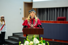 Osoba w stroju akademickim przemawia przy mównicy podczas uroczystości dyplomowania absolwentów.