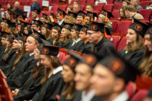 Grupa absolwentów w togach i biretach siedzi w rzędach podczas uroczystości rozdania dyplomów.
