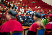 Osoby w oficjalnych togach siedzą w pierwszych rzędach podczas dyplomatorium