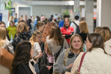 The photo shows a dozen or so people in a bright hallway during the event. People are standing in groups and talking. In the background, there are stands with banners, plants, and marble pillars.
