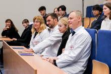 Kobiety i mężczyźni siedzą w sali wykładowej. w pierwszym rzędzie cztery osoby, z których trzy mają na sobie białe fartuchy lekarskie.