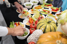 Stół z różnorodnymi świeżymi warzywami oraz talerzykami z pokrojonymi warzywami i sosem do maczania. Na stole znajdują się m.in. pomidory, papryki, ogórki, sałata, dynie i kabaczki.