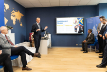 Uczestnicy oficjalnego otwarcia Welcome Center. Stoją po lewej i po prawej stronie, w jasnym pomieszczeniu. Część osób jest elegancko, część nieformalnie ubrana. Na ścianie widać duży ekran z prezentacją multimedialną.