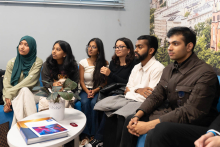 Grupa młodych osób, różnego pochodzenia, ubranych nieformalnie. Siedzą na kanapie. Patrzą przed siebie. Przed nimi stoi stolik.