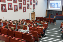 A lecture in an auditorium with red seats. A slide titled “Modern Cardiology Therapies” is displayed on the screen. Young people are sitting and raising their hands.