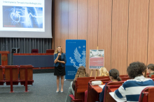 A person is speaking on stage in the auditorium. On the screen is a slide titled “Intensive Cardiac Care” with an image of a heart.